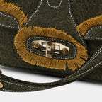 Close up of fringe flap and gold rotating lock on Purpleberry Luna green denim sling bag